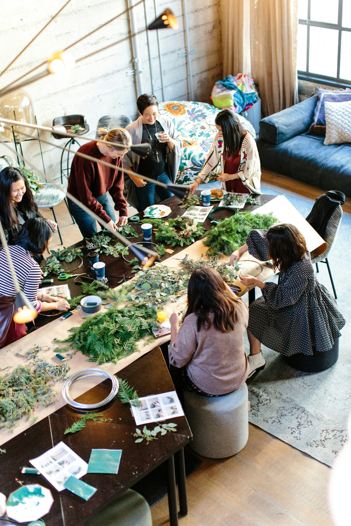 From our vantage point above, we see a group of conscious business owners and women creating crafts using fresh foliage in a warm and airy room.
