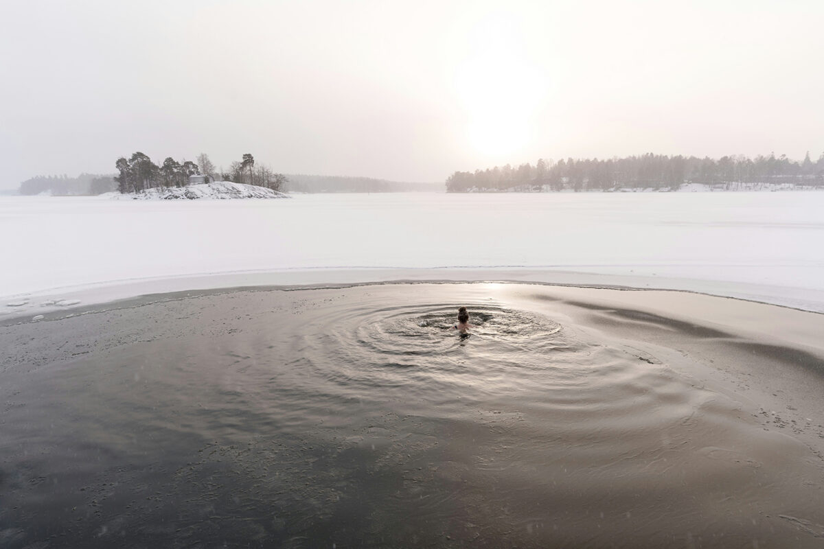 A snowy and hazy landscape with a big lake in the middle; inside a midlife woman takes a plunge